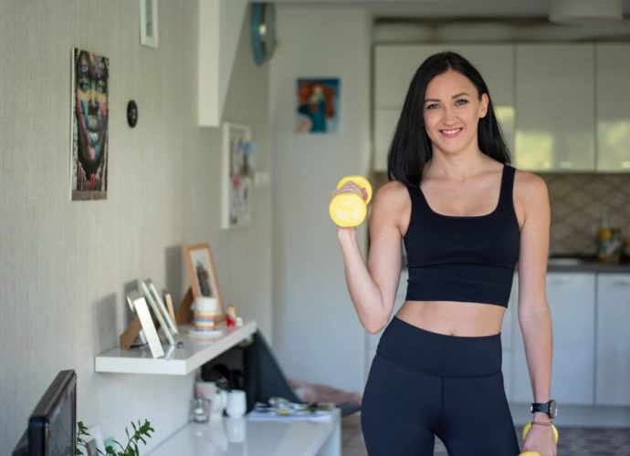 Smiling woman in activewear lifting dumbbells at home for a healthy lifestyle.