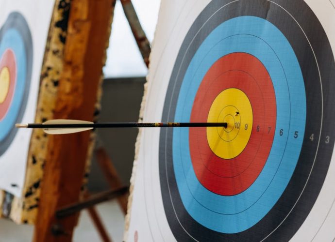 An arrow hits the bullseye on a colorful target in an indoor archery range.